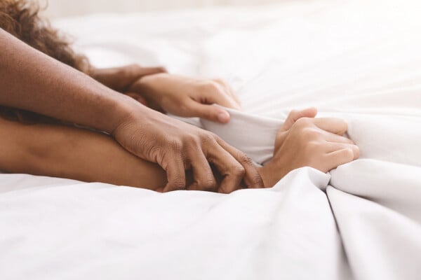 Mãos de casal puxando o lençol durante relação sexual