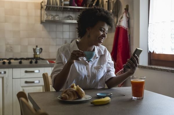 Mulher tomando café da manhã enquanto olha o celular