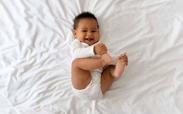 foto de bebê deitado na cama com as mãos nos pés e sorrindo