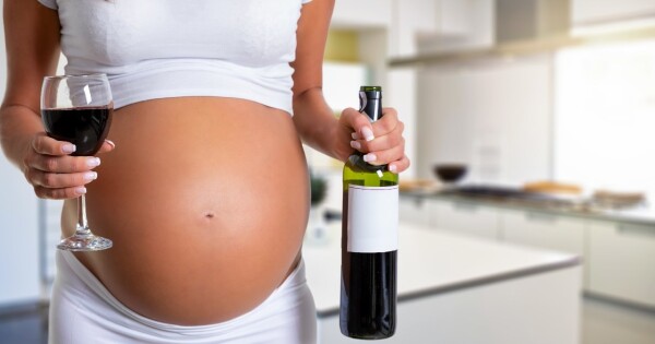 Grávida segurando garrafa e taça de vidro com vinho
