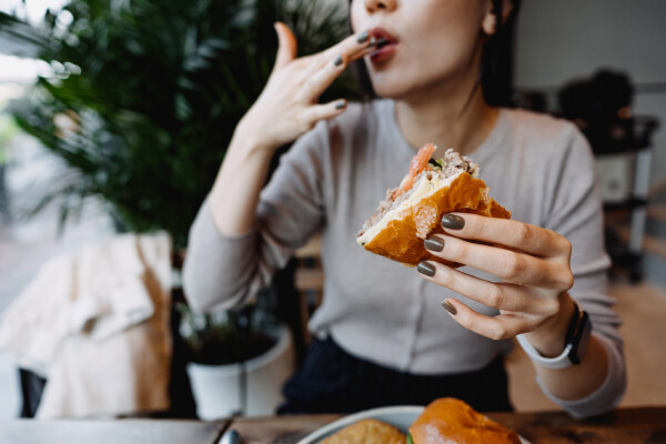 mulher sentada em mesa segurando um hambúrguer em uma mão enquanto lambe os lábios