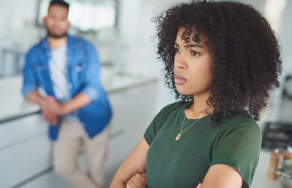 Mulher negra brava em primeiro plano, em segundo plano um homem observa