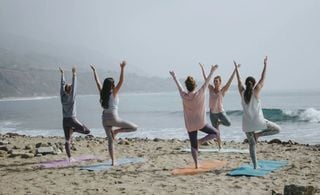 Um grupo de cinco pessoas praticando yoga na praia