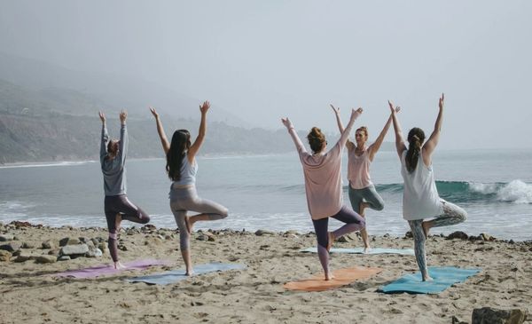 Um grupo de cinco pessoas praticando yoga na praia