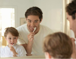 Pai e filho escovando os dentes em frente ao espelho