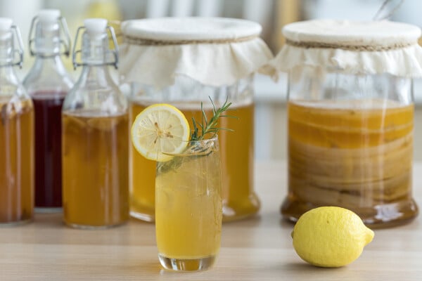 Chá de kombucha com limão e raiz adoçada preenchendo jarra de vidro no fundo da cozinha