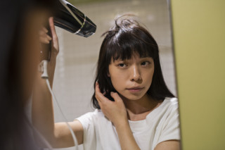 Mulher em frente ao espelho secando o cabelo com um secador em uma mão