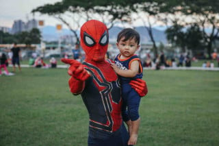 Pessoa fantasiada de homem-aranha segurando criança nos braços