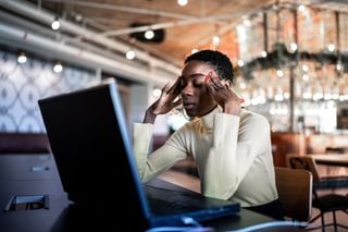 Mulher em frente a um notebook com as mãos na cabeça, com síndrome de burnout