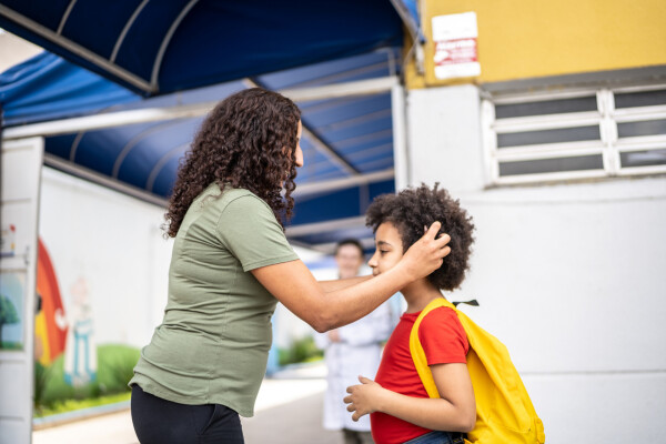 Mãe com a mão no cabelo da filha em frente à porta da escola