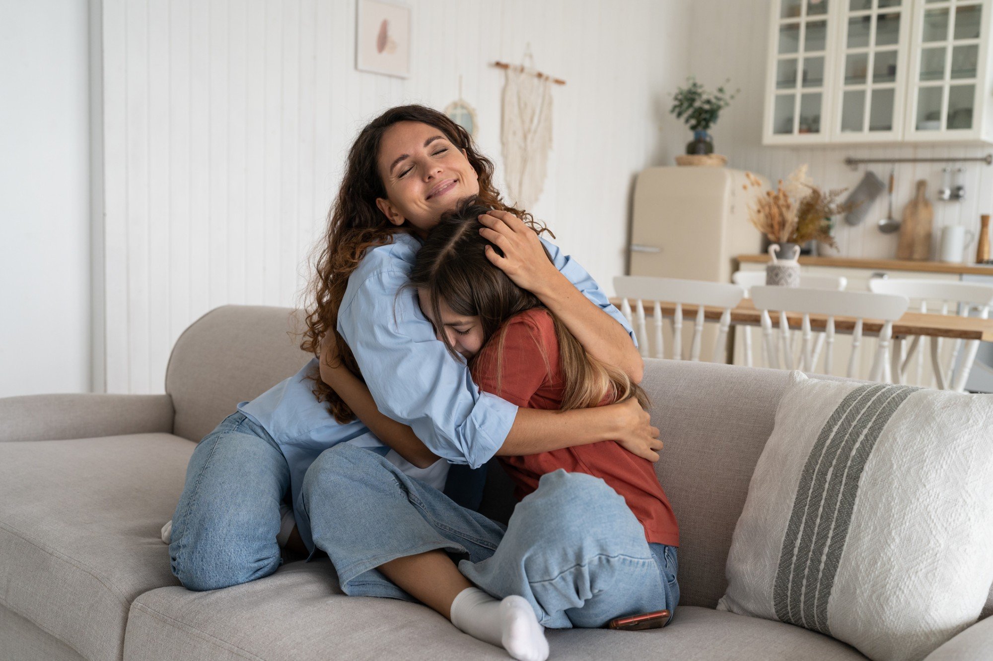 Mãe e filha abraçadas enquanto estão sentadas no sofá