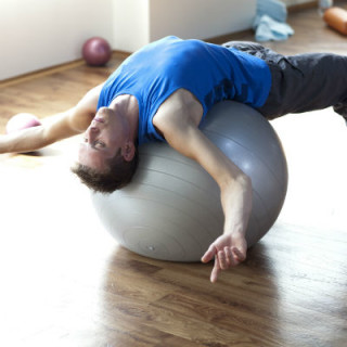 Homem se alongando sobre a bola grande de pilates - Foto: Getty Images