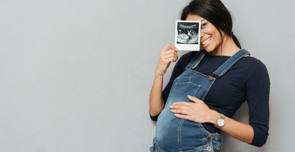 Mulher grávida segurando uma foto e sorrindo para a câmera