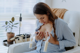 Mulher sentada em poltrona com bomba extratora de leite dupla nas mamas extraindo leite materno