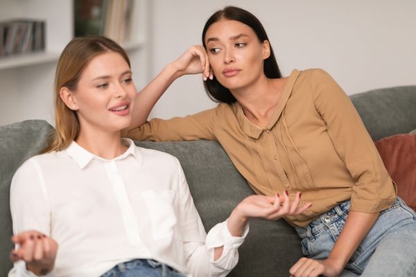 Mulher incomodada com outra mulher sentada no mesmo sofá
