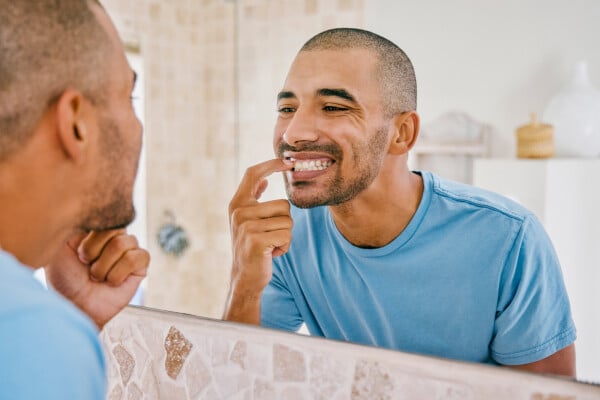 Homem olhando os dentes no espelho do banheiro