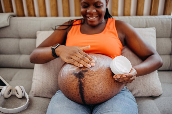 Mulher grávida passando um creme na barriga enquanto segura o pote com uma mão