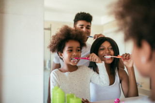 Homem, mulher e menina escovando os dentes em frente ao espelho