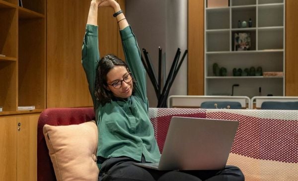 Mulher sentada em um sofá com um notebook no colo se espreguiçando