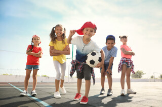Grupo de crianças com menino na frente segurando uma bola de futebol