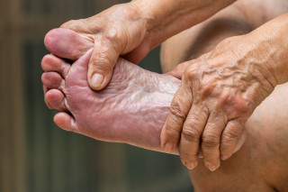 Pessoa segurando o pé direito com as duas mãos enquanto apoia o tornozelo na perna esquerda