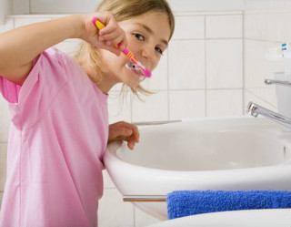 Criança escovando os dentes na beirada da pia do banheiro