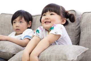 Duas crianças japonesas assistindo TV, sentadas no sofá