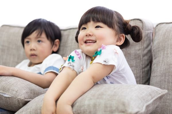 Duas crianças japonesas assistindo TV, sentadas no sofá