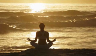 Jovem medita enquanto toma sol na praia - Foto: Getty Images
