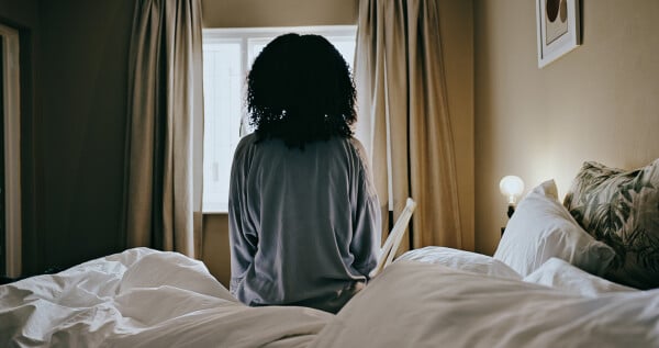 imagem de mulher de costas sentada em cama e de frente para uma janela