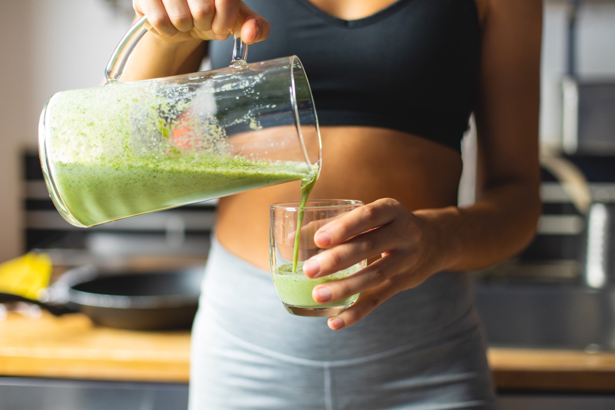 Imagem aproximada de mulher despejando vitamina em copo de vidro