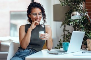 Mulher em frente ao computador enquanto come um iogurte