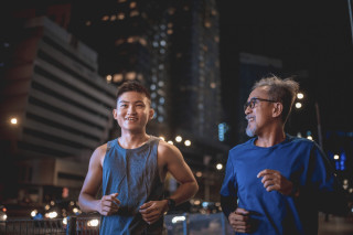 Jovem asiático correndo em uma avenida, à noite, ao lado de um senhor asiático