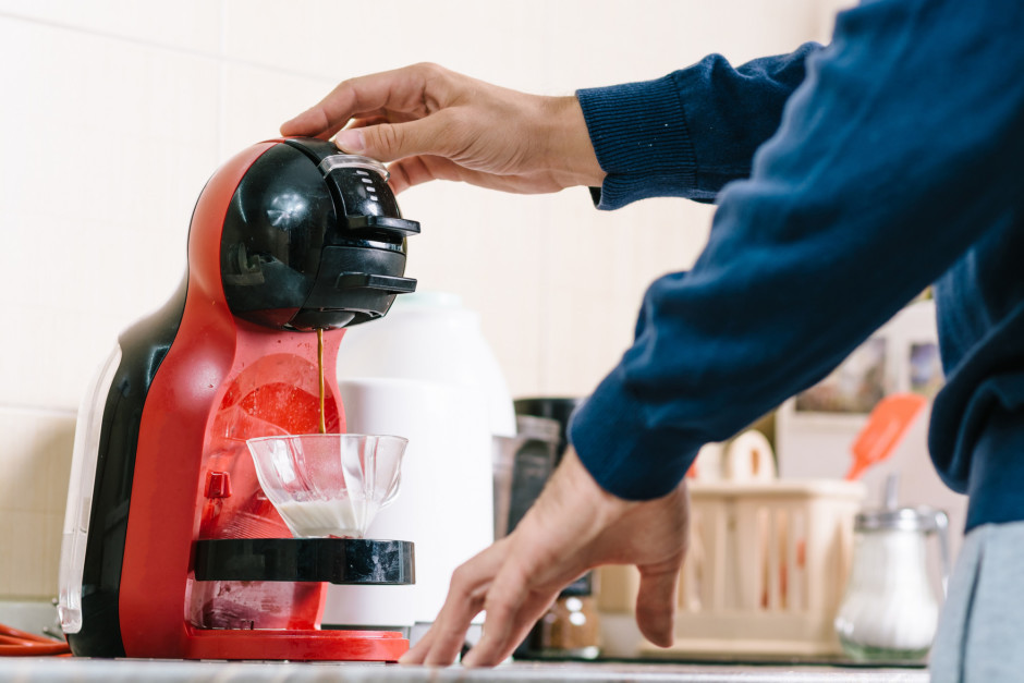 Homem com a mão em uma cafeteira vermelha enquanto ela faz café