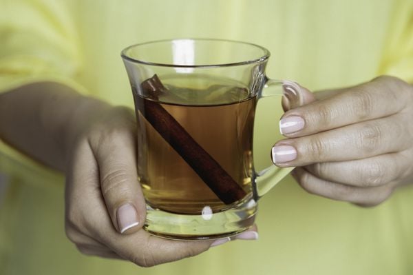 imagem aproximada das mãos de uma mulher segurando um copo de vidro com chá de canela