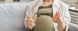 Mulher grávida segurando um comprimido e um copo d'água