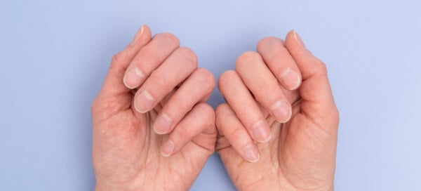 Mãos femininas mostrando as unhas sob fundo azul claro
