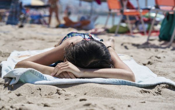 Mulher se bronzeando, deitada na areia da praia