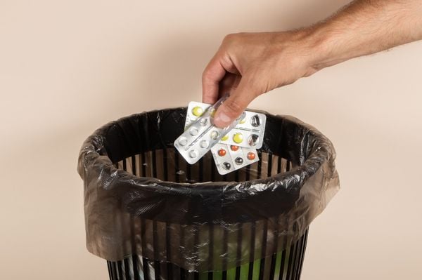 Imagem aproximada de mão colocando cartelas de medicamentos em lixeira