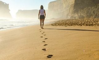 Mulher caminhando na praia e deixando pegadas na areia