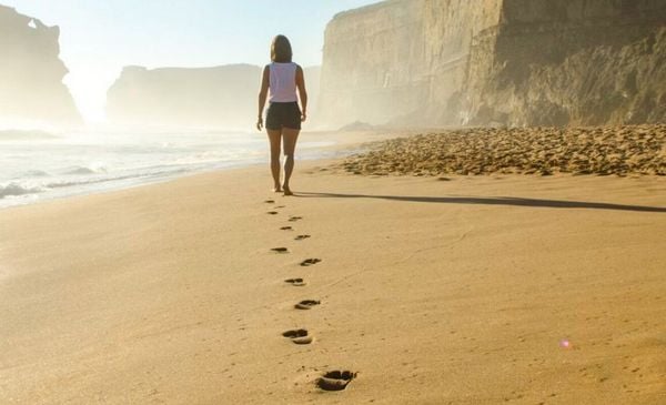 Mulher caminhando na praia e deixando pegadas na areia