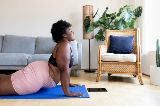 Mulher fazendo ioga no tapete em casa com um tablet na frente