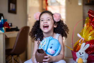 Criança segurando um ovo de páscoa de chocolate enquanto abraça um coelho da páscoa azul