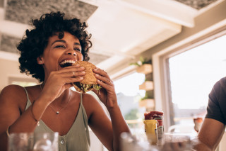 Mulher comendo um hambúrguer sorrindo