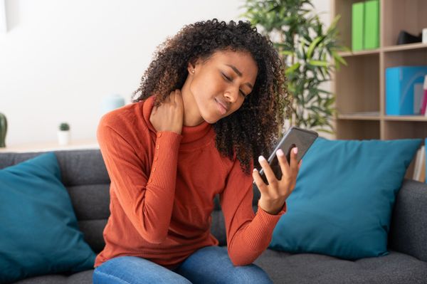 Mulher com dor no pescoço segurando celular