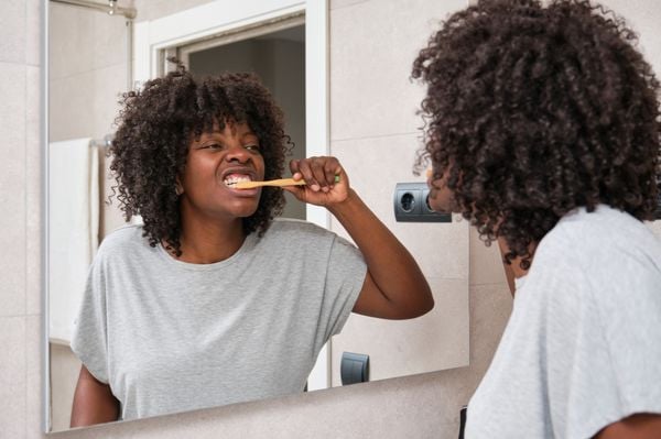 mulher negra de frente para o espelho escovando os dentes