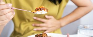 foto de mulher comendo um prato de comida com a mão no estômago