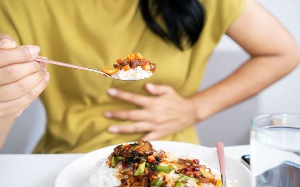 foto de mulher comendo um prato de comida com a mão no estômago