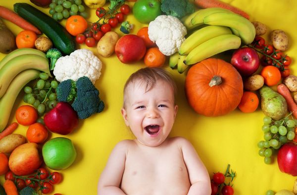 Bebê sorridente cercado por alimentos naturais