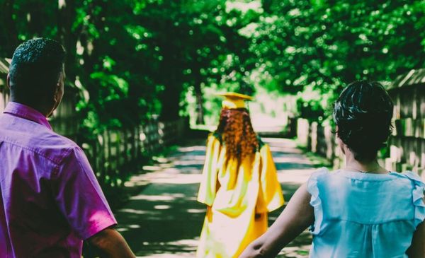 Casal de pais negros de mãos dadas olhando a filha andando a frente